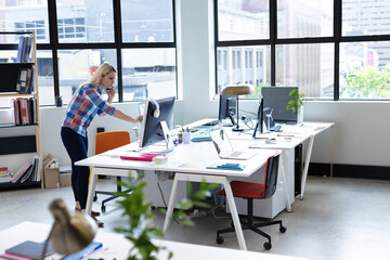 White desks hosting laptops and potted plants beside large windows overlooking cityscape in office