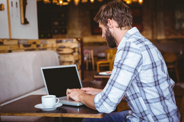 Silver laptop sitting on wooden table with white coffee cup resting beside in cozy café © WavebreakMediaMicro