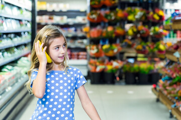 Female child holding banana like phone in supermarket produce aisle with flower displays