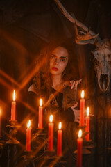 Gothic woman in black dress posing as a queen on anceint throne in candlelight on dark background.
