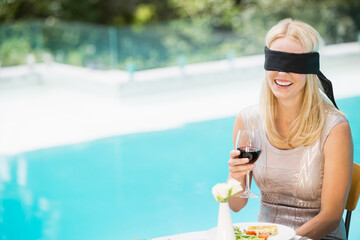 Glass of red wine resting on tabletop beside salad plate and white flower near turquoise pool