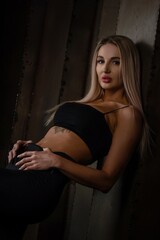 Fototapeta premium Beautiful sexy blonde woman model in black pants and black top posing on metal wall background.