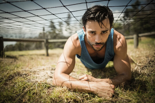 Fototapeta Athlete crawling under low rope net obstacle on sunlit grassy field near wooden fence
