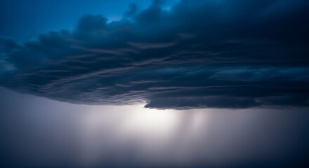 Fototapeta premium Brooding storm clouds gather, their dark forms contrasting with the faint, ethereal glow below them.
