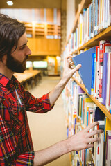 Man is sliding blue hardcover book from shelf in library room while wearing red plaid shirt