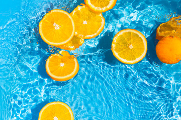 Creative summer composition made of sliced orange in transparent pool water with splashes. Refreshment concept. Healthy refreshing drink theme. Top view