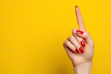 A hand with red nails pointing a finger upward against a yellow background
