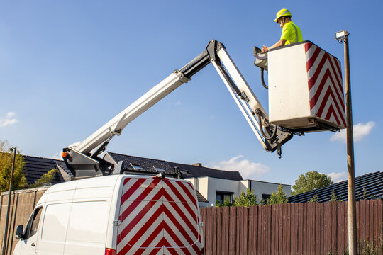 A technician in a bright vest works at height using a hydraulic boom lift truck near private homes. Concept of occupational safety and technical work. - Powered by Adobe