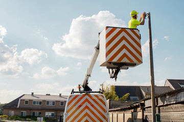 Utility worker in a high-visibility vest repairs a street light using a lift truck on a residential...