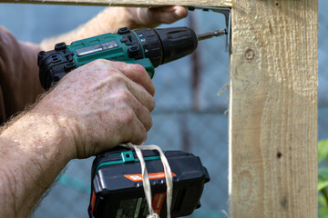 Hands of man using drill to assemble wooden structure. Close-up.