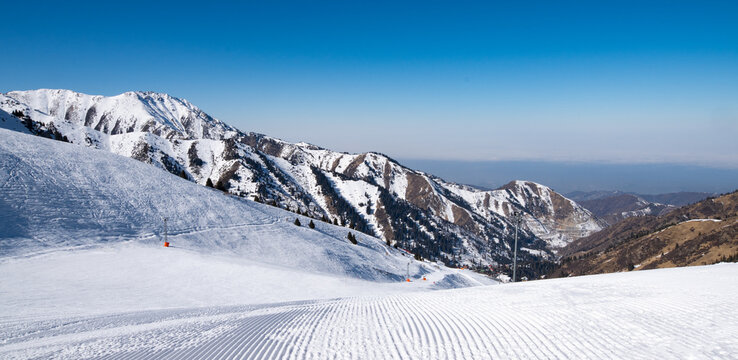 Famous Shymbulak mountain ski resort view with beautiful white and snowy ski lines, cable-way, blue sky, fresh air. Wonderful picturesque resort for holidays and travelling near Almaty