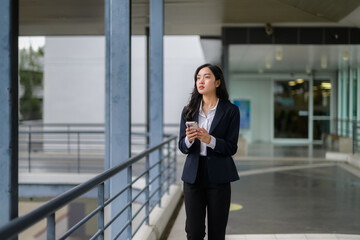Fototapeta premium Young Asian manager walking in a modern office building while using her smartphone