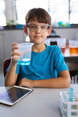 Transparent beaker holding blue liquid sitting on bench with tablet computer in science lab