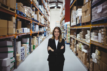 Businesswoman inspecting inventory in warehouse aisle with metal shelving and pallets