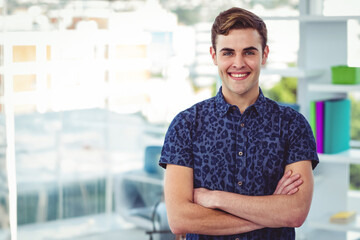 Man standing with arms crossed at office desk by window showing urban skyline, shelving unit