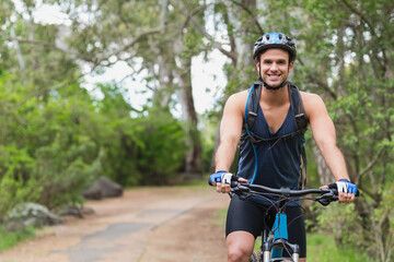 Man riding mountain bike on dirt trail in forest wearing cycling helmet and hydration backpack