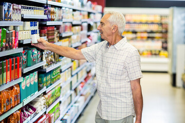 Senior male shopper grabbing carton from supermarket shelving near fridge display, copy space