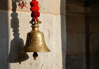 Obraz premium brass temple bell hanging on a wall with warm sunlight illuminating its ornate design and creating a serene atmosphere in a spiritual setting