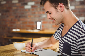 Man writing in notebook with pen at brick-walled cafe table with coffee cup, copy space