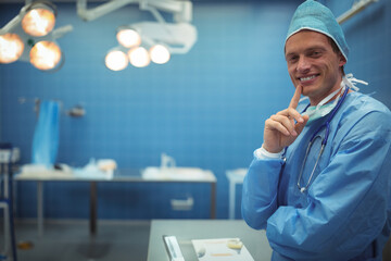 Mid adult male surgeon leaning against steel table in operating room with stethoscope, copy space