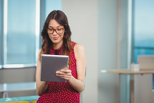 Woman wearing glasses and red polka-dot blouse holding tablet sitting at desk in modern office