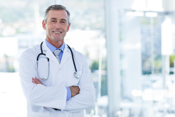 Male doctor standing with arms crossed with stethoscope near large windows overlooking city skyline