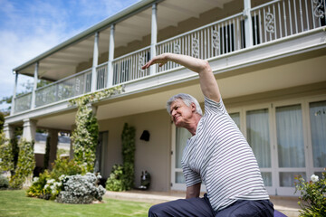 Senior man balancing on exercise ball stretching sideways on lawn by porch pillars, copy space