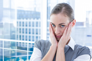Woman standing on balcony holding cheeks gazing at reflective office towers through glass railing