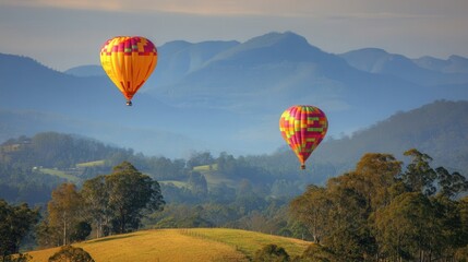 Two colorful hot air balloons soar above a landscape of hills and valleys.