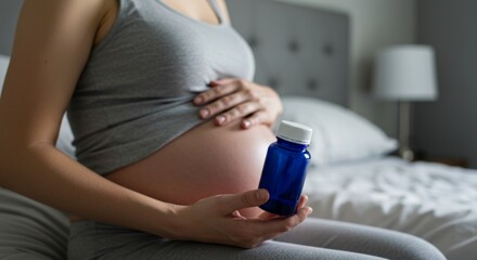 Expectant mother in gray tank top is seated on bed, holding blue supplement bottle, emphasizing importance of health and nutrition during pregnancy journey	