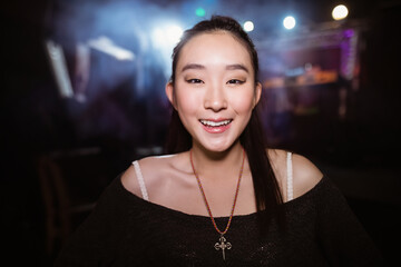 Chinese woman standing in dim event space with lights wearing black top with beaded cross necklace