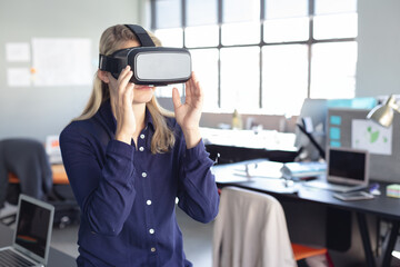 Virtual reality headset sitting on desk among monitors laptops papers in bright open office