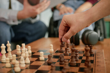 Caucasian man with disability playing chess with another man, close up of hands moving chess pieces on wooden board, wheelchair visible in background, celebrating birthday