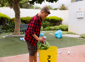 Plastic bottles and green reusable bag being placed into yellow recycling bin on patio