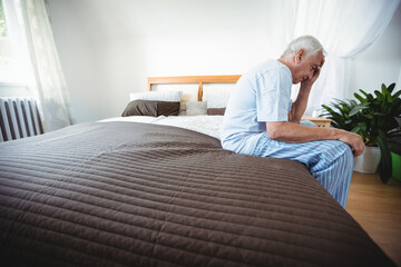 Brown quilted coverlet lying on bed beside radiator under sheer drapes filtering soft daylight