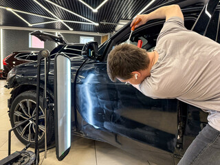 Process of paintless dent repair on car body. The mechanic at the auto shop with tools to repair...