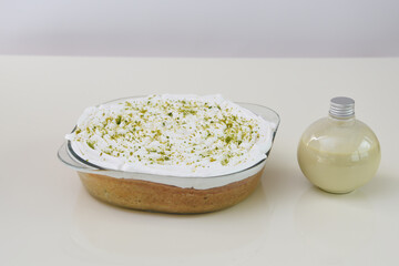 Key Lime Pie in a clear glass baking dish topped with whipped cream and dusted with bright green lime zest with a bottle of sauce dip side view of classic dessert