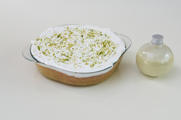 Key Lime Pie in a clear glass baking dish topped with whipped cream and dusted with bright green lime zest with a bottle of sauce dip side view of classic sweet dessert
