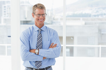 Fototapeta premium Adult male standing arms crossed before office windows wearing eyeglasses striped tie wristwatch