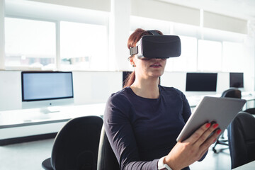 Virtual reality headset and tablet resting on black swivel chair in bright computer lab, copy space