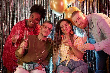 Diverse group of young adults celebrating birthday, smiling and holding champagne glasses, two people sitting in wheelchairs with disability, festive balloons and decorations in background