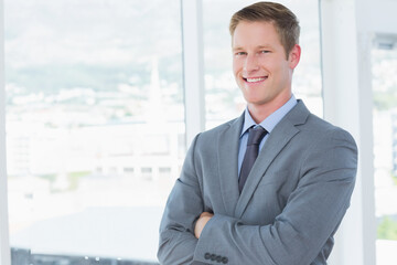 Corporate executive standing with arms crossed before floor-to-ceiling windows showing city skyline