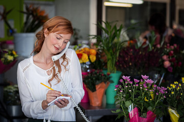 Corded telephone handset ringing beside notepad and pencil in floral shop among plants and bouquets