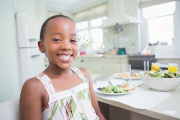African American child girl sitting at kitchen table eating salad and drinking juice, copy space © WavebreakMediaMicro
