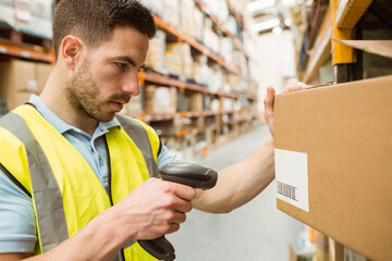 Male worker wearing safety vest scanning barcode with scanner on box in warehouse aisle, copy space
