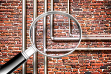 Water and gas pipeline in front of an old brick wall - Concept image seen through a magnifying glass