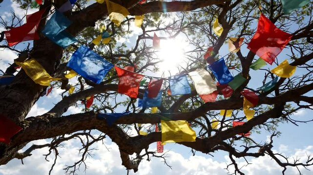 Colorful prayer flags hanging on a tree against sunlight with a beautiful blue sky backdrop