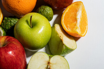 Close-up of mixed fresh fruits with apples, orange slices, and kaffir limes on white background