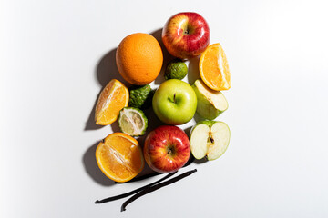Flat lay of whole and cut apples, oranges, kaffir limes, and vanilla pods on white background with shadows