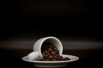 Coffee cup full of beans lying on the saucer on a black background